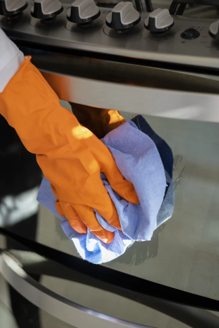 Hands cleaning oven glass with cloth and gloves Hands cleaning oven glass with cloth and gloves